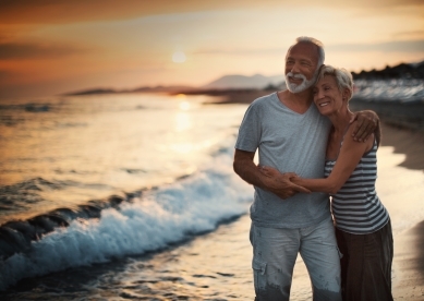 Senior couple walking on the beach by the water at sunset